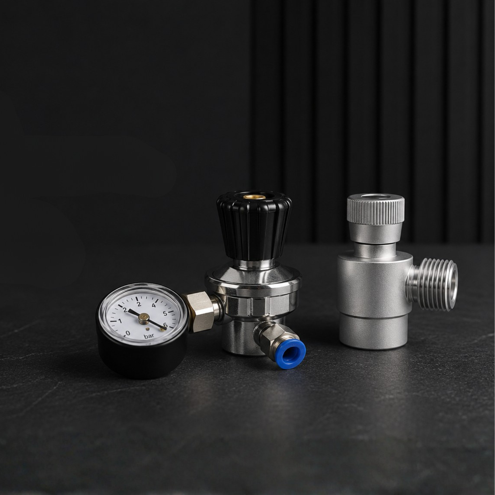 Three metal components including a pressure gauge, valve, and connector on a dark surface.