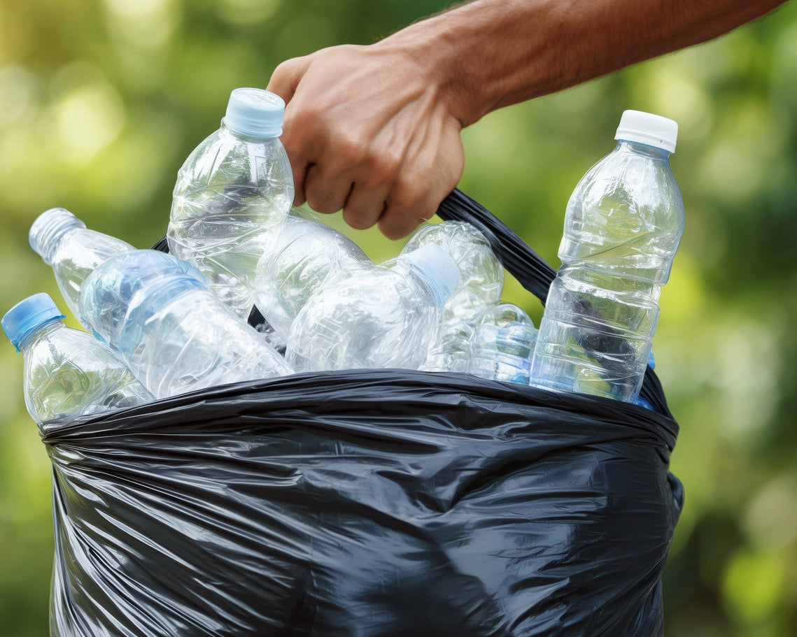 Person holding a black trash bag filled with plastic bottles against a blurred green background