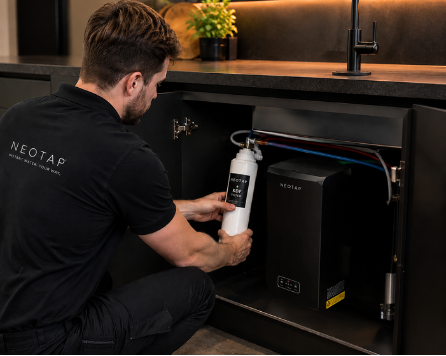 Person installing a NEOTAP water filtration system in a kitchen.
