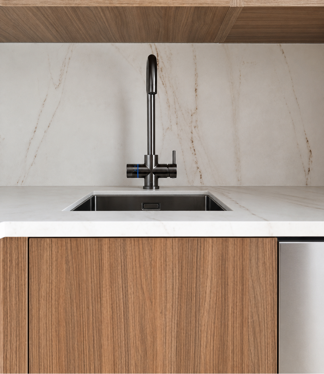 A modern kitchen faucet in matte black, mounted over a white marble countertop with a matching marble backsplash and wood cabinetry.